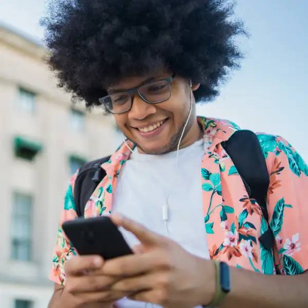 A young man with an afro smiles while using his phone, showcasing a joyful moment of connection