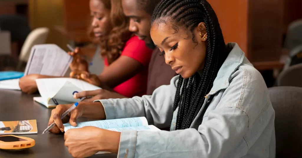 Three students studying together in a library with information about bursaries for 2025